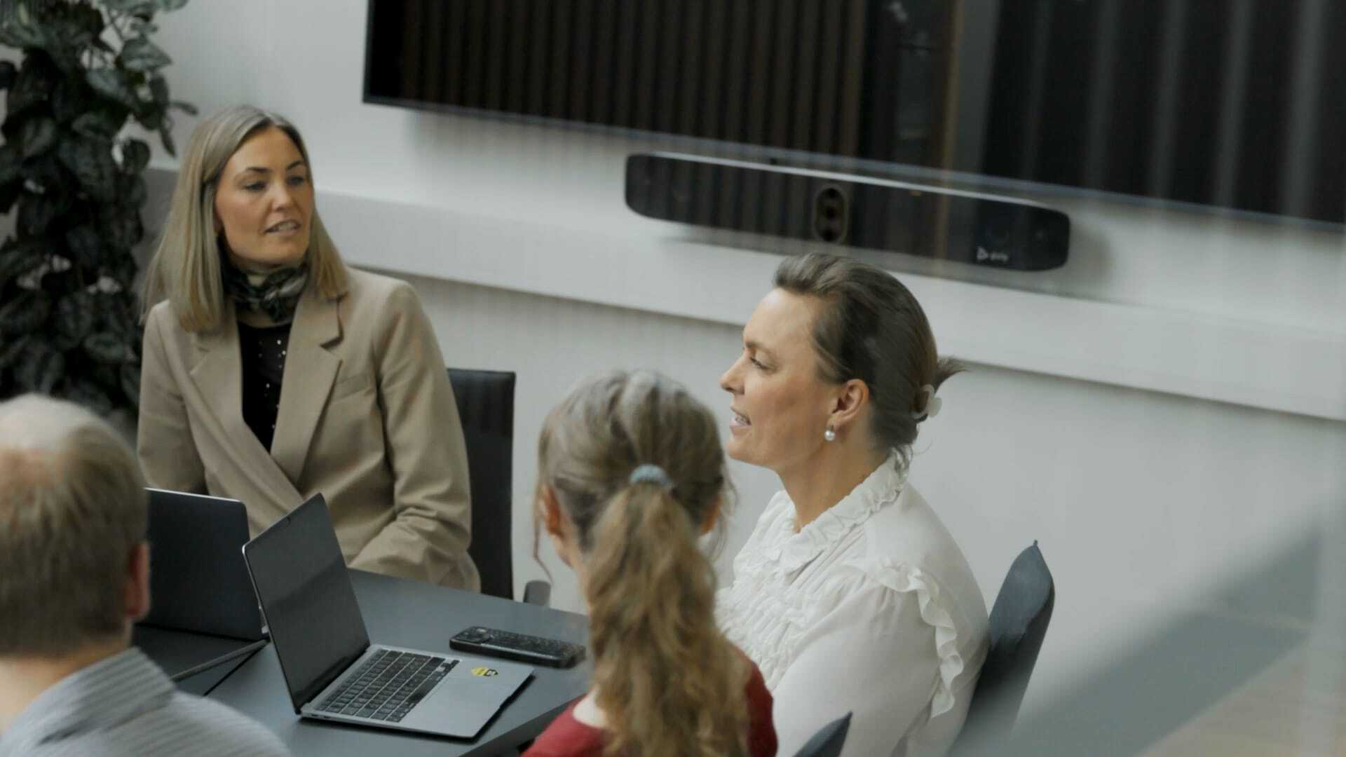 Kolleger i møde ved konferencebord med laptops og præsentationsskærm