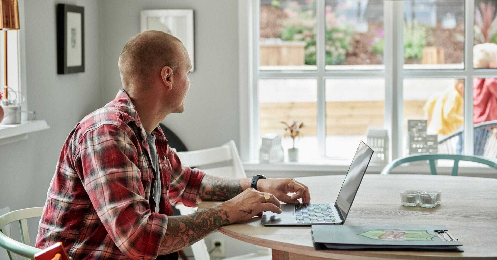 Person sidder ved et spisebord med en bærbar computer og arbejder
